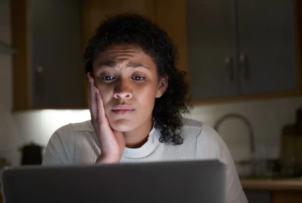 woman holding her cheek in pain and looking at her laptop due to leaving a missing molar tooth untreated